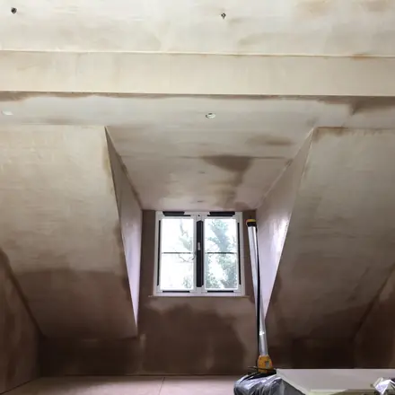 A loft room skimmed out to bare pink plaster, the sloping dormer cheeks meeting the ceiling in crisp straight arrises around a small window.