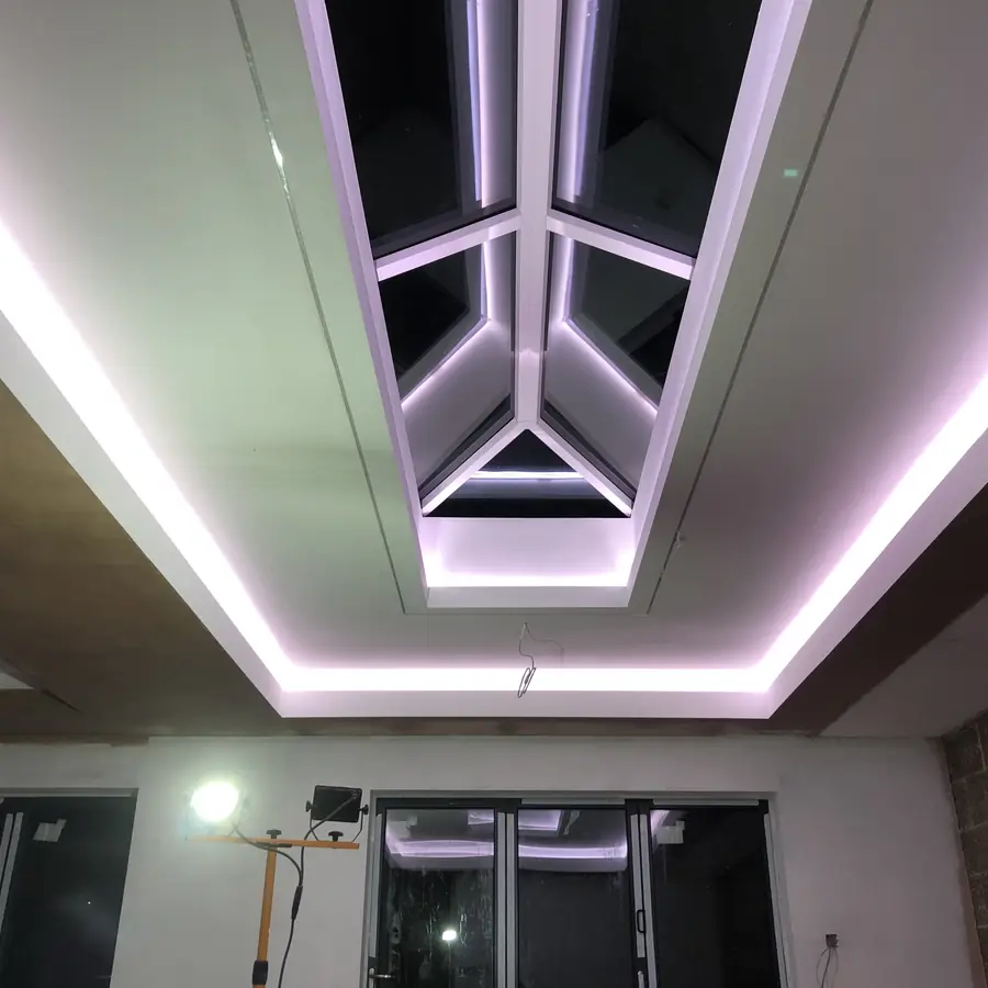 A dropped ceiling plastered around a roof lantern, a continuous lit shadow gap tracking its perimeter in a sharp angular border.