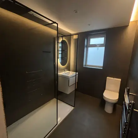 A finished shower room lined wall, floor and ceiling in dark micro cement, with a frameless glass screen and a wall-hung basin.